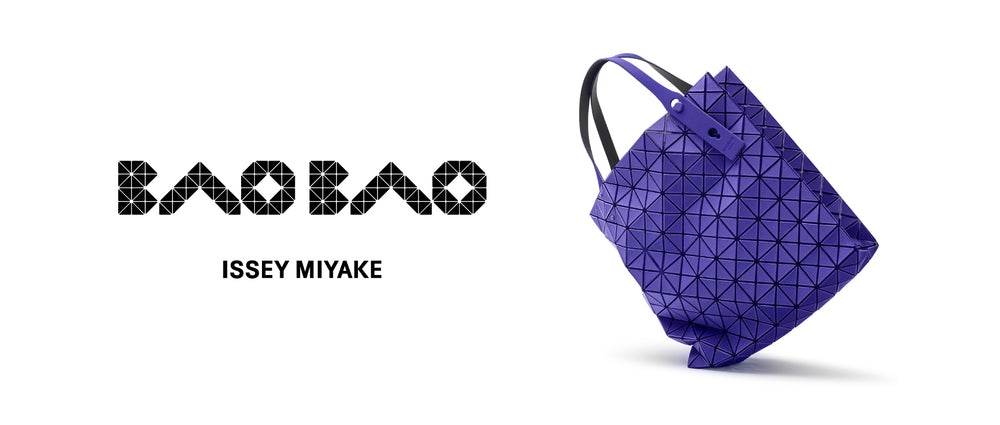 White background. Left: BAO BAO ISSEY MIYAKE logo in black. Right: PRISM PLUS tote bag in blue standing on one corner, tilted.