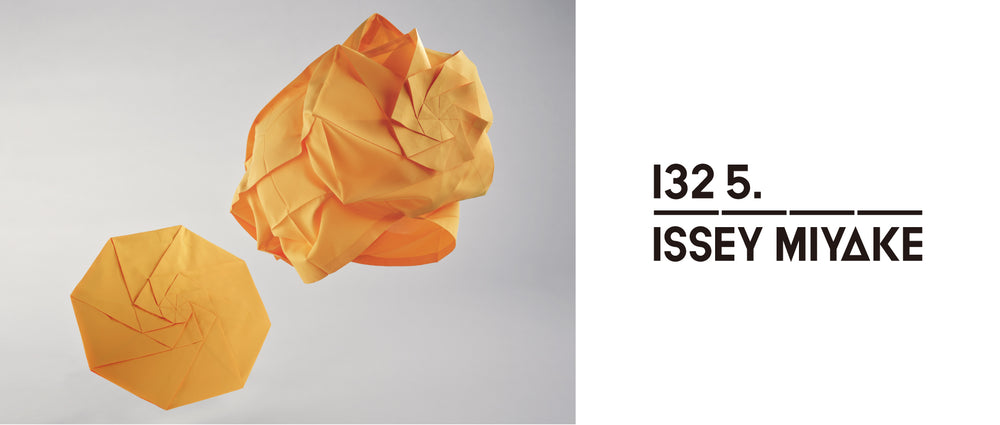 Left: Two NO.7 tops in marigold suspended in mid air. One folded flat in a circular shape and one unfolded in a spherical shape. Against light grey background. Right: 132 5. ISSEY MIYAKE logo in black on white background. 
