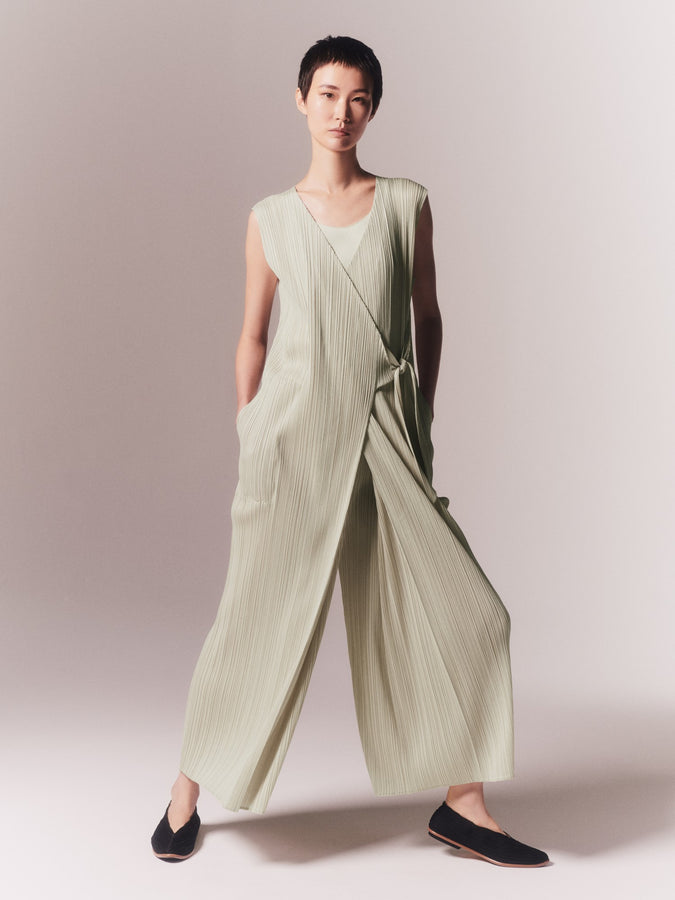 Model wearing JAM jumpsuit in off white, standing with hands in her pockets and legs spread apart. Wearing pleated ballet flats in black.