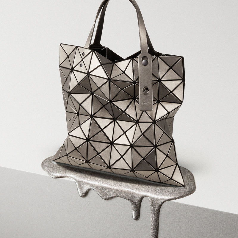 LUCENT METALLIC Tote bag in Silver standin in puddle of silver paint on light grey background.