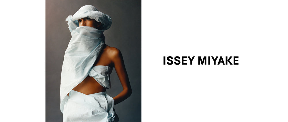 Left: Photo of a model wearing bandeau top and skirt from TWISTED in light blue. Paired with matching hat with attached scarf. Right: ISSEY MIYAKE logo in black on white background.