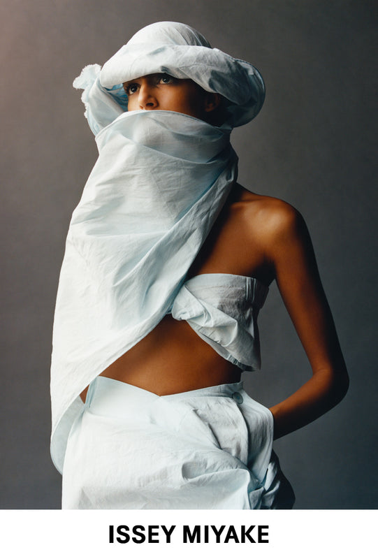 Top: Photo of a model wearing bandeau top and skirt from TWISTED in light blue. Paired with matching hat with attached scarf. Bottom: ISSEY MIYAKE logo in black on white background.