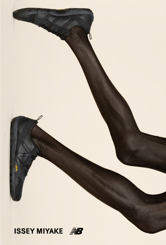 Main: Legs wearing black sneakers, posing against a light yellow background. Bottom left corner: ISSEY MIYAKE and New Balance logos in black.