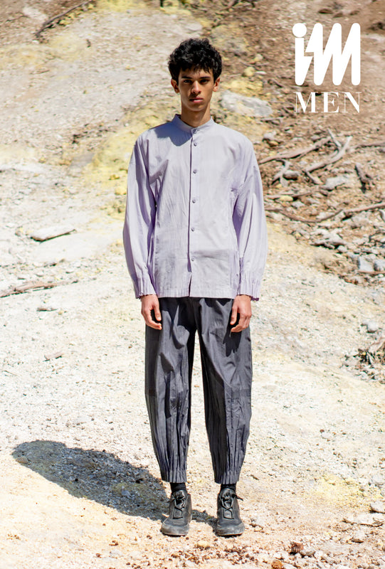 Model wearing DUO SHIRT in lavender with dark purple DUO trousers and black sneakers. Desert background. IM MEN logo in white in top-right corner.